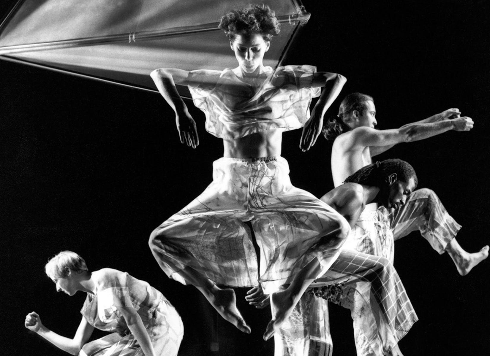 A dancer with light skin jumps, looking downward, in front of three other dancers.