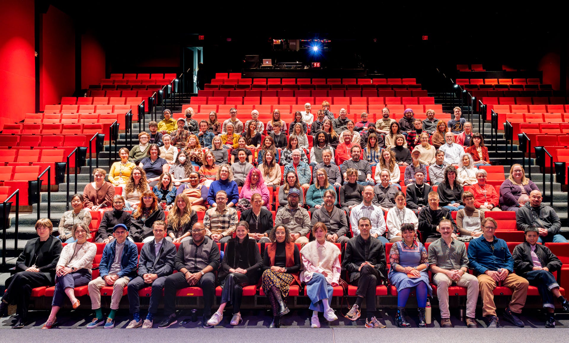 A large group of adults sitting in an auditorium with red seats, facing the viewer