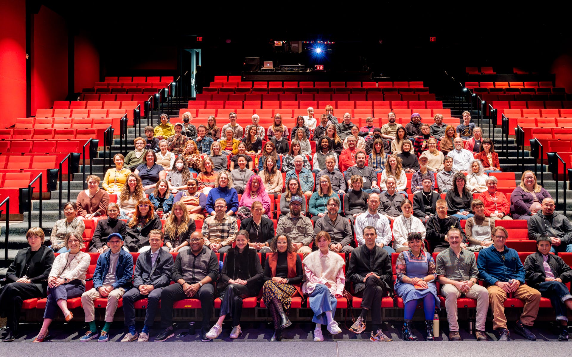 A large group of adults sitting in an auditorium with red seats, facing the viewer