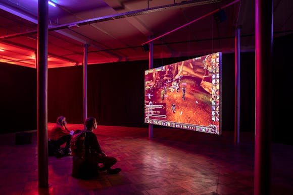 Two people sit on the floor in front of a hanghing projection of World of Warcraft game.