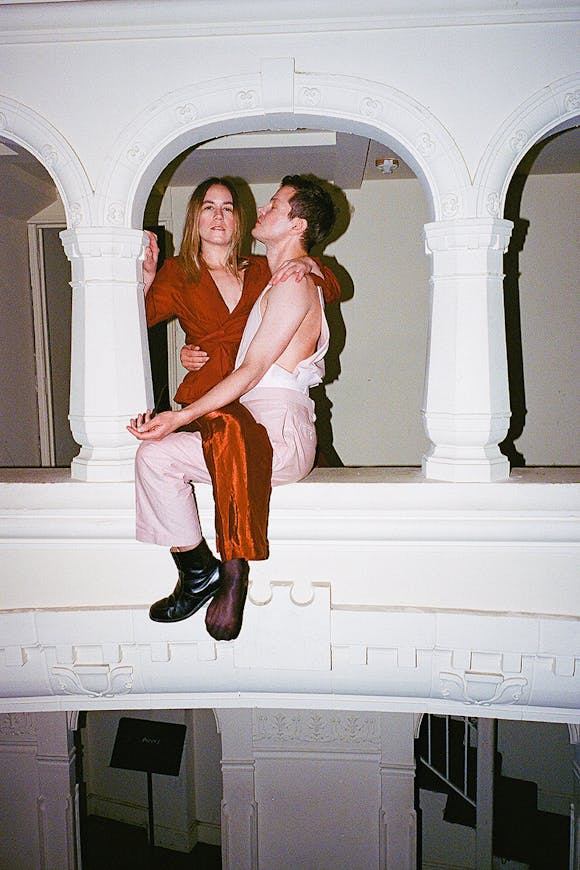 Kate Wallich and Perfume Genius sitting on the ledge of a balcony.