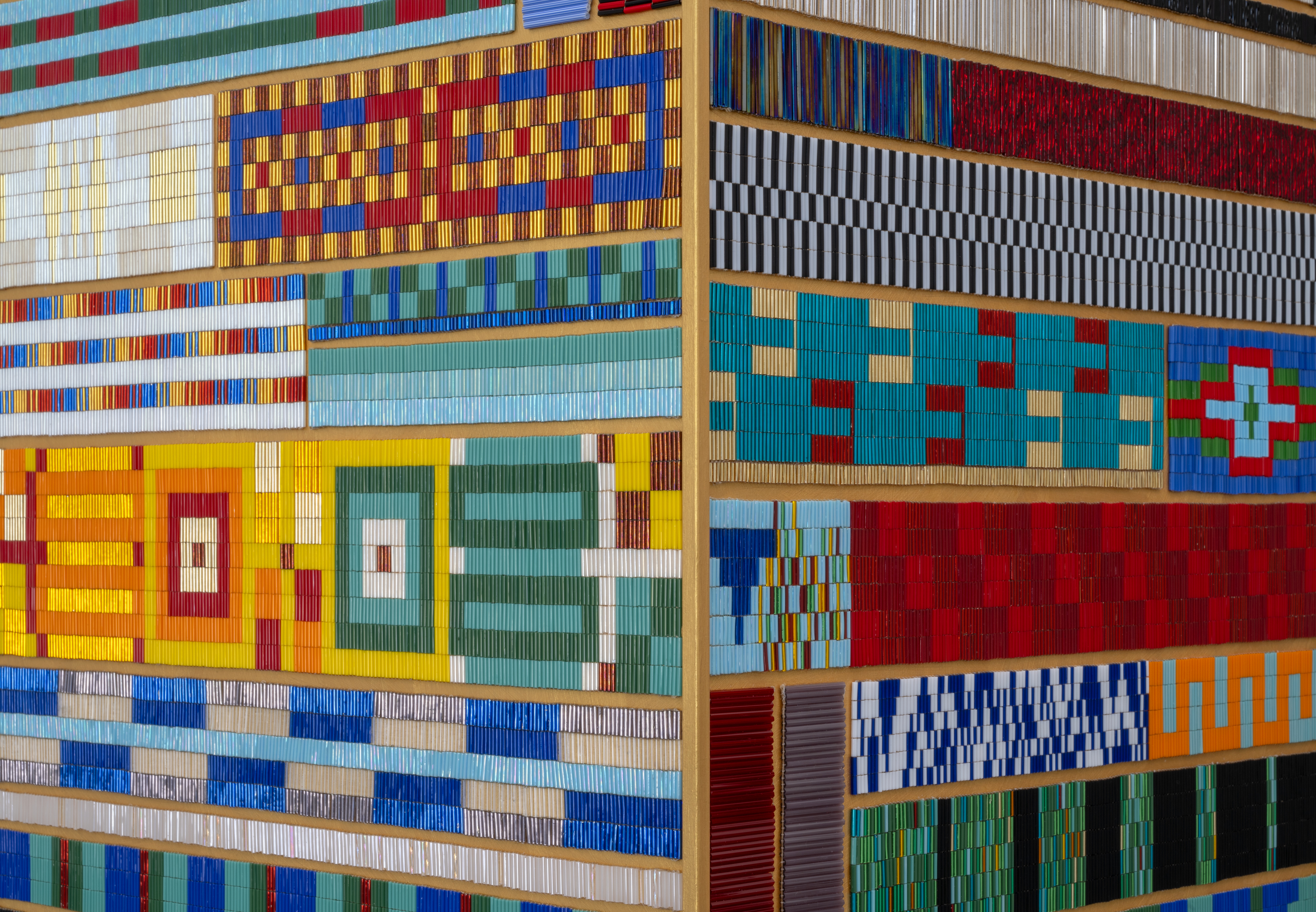 A close up on a patchwork of beaded panels. Each is sewn into different geometric patterns, many are highly reflective