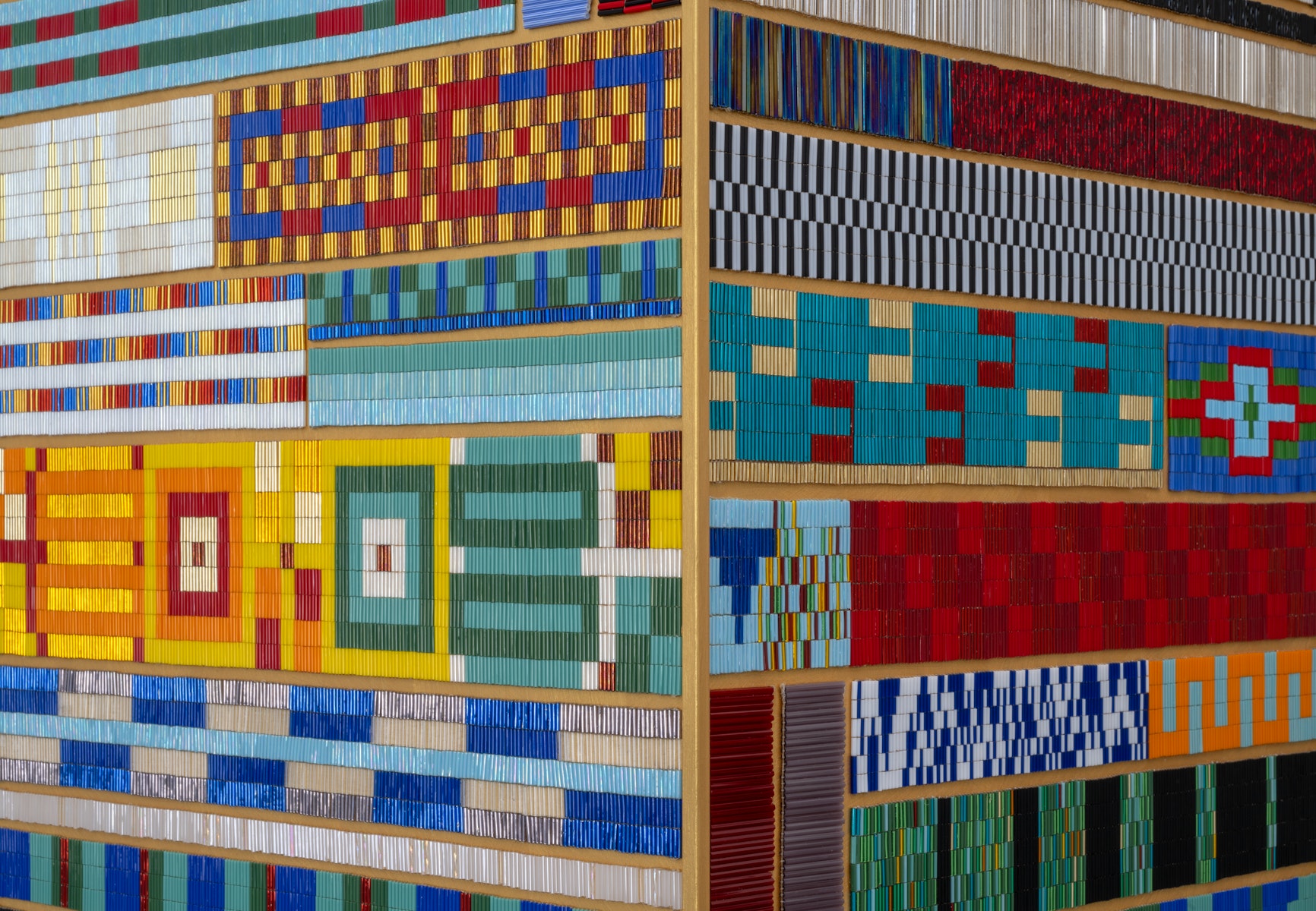 A close up on a patchwork of beaded panels. Each is sewn into different geometric patterns, many are highly reflective