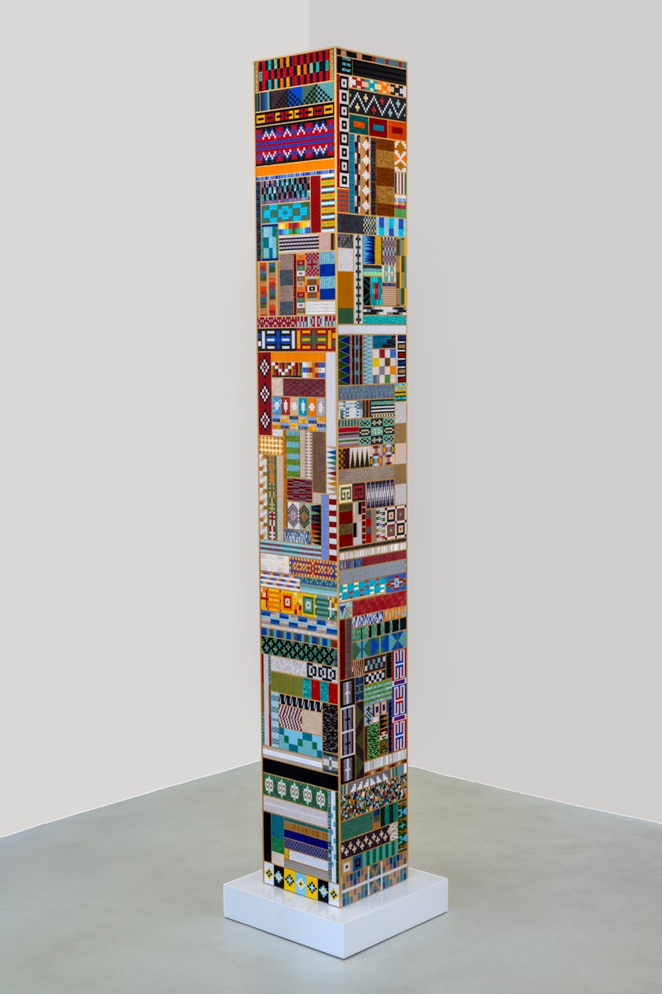 A large columnar sculpture made up of a patchwork of beaded panels. Each is sewn into different geometric patterns, many are highly reflective
