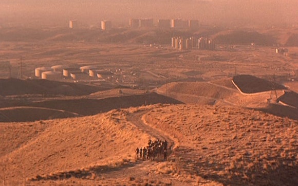 Desert with a city in the background and a group of people walking in the foreground.