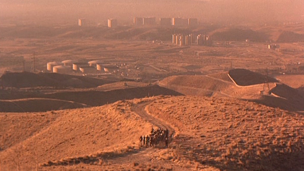 Desert with a city in the background and a group of people walking in the foreground.