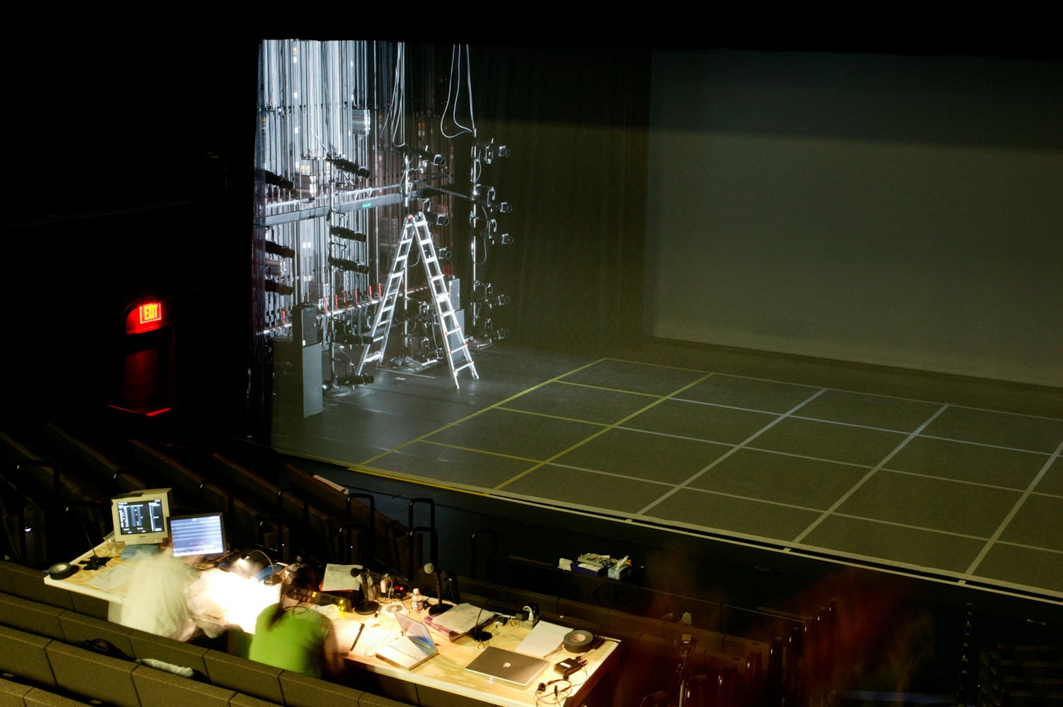Technicans ready lighting from a control panel in the audience within a large theater.