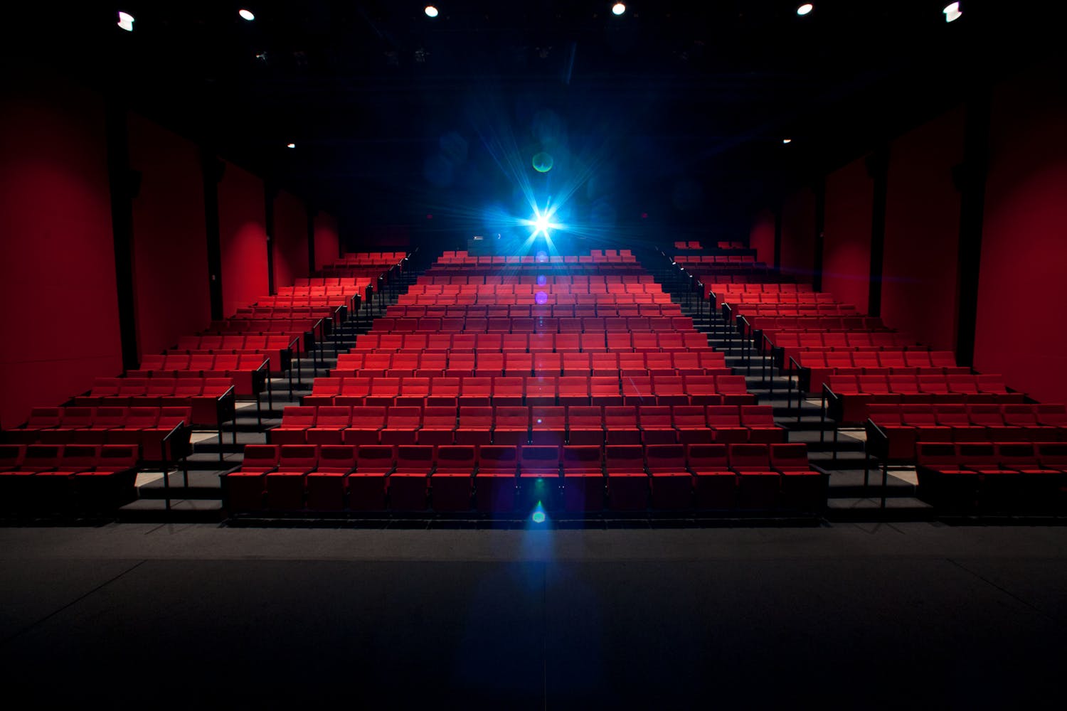 Interior cinema with red chairs from stage with projector light shining.