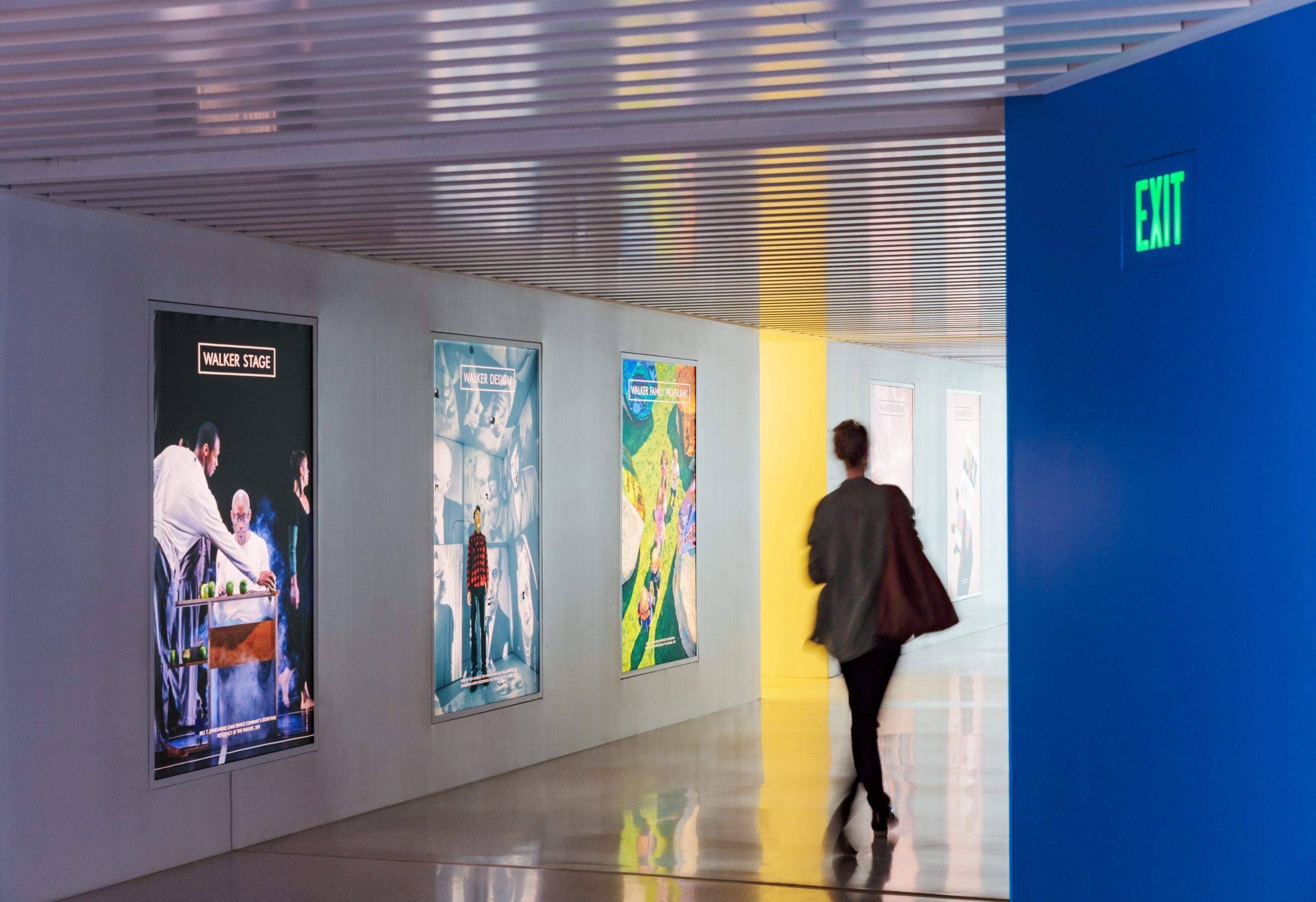 A woman walks down a hallway with posters advertising museum programming.