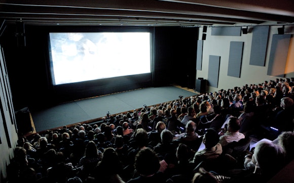 An audience sits in seats watching a film projected in a cinema.
