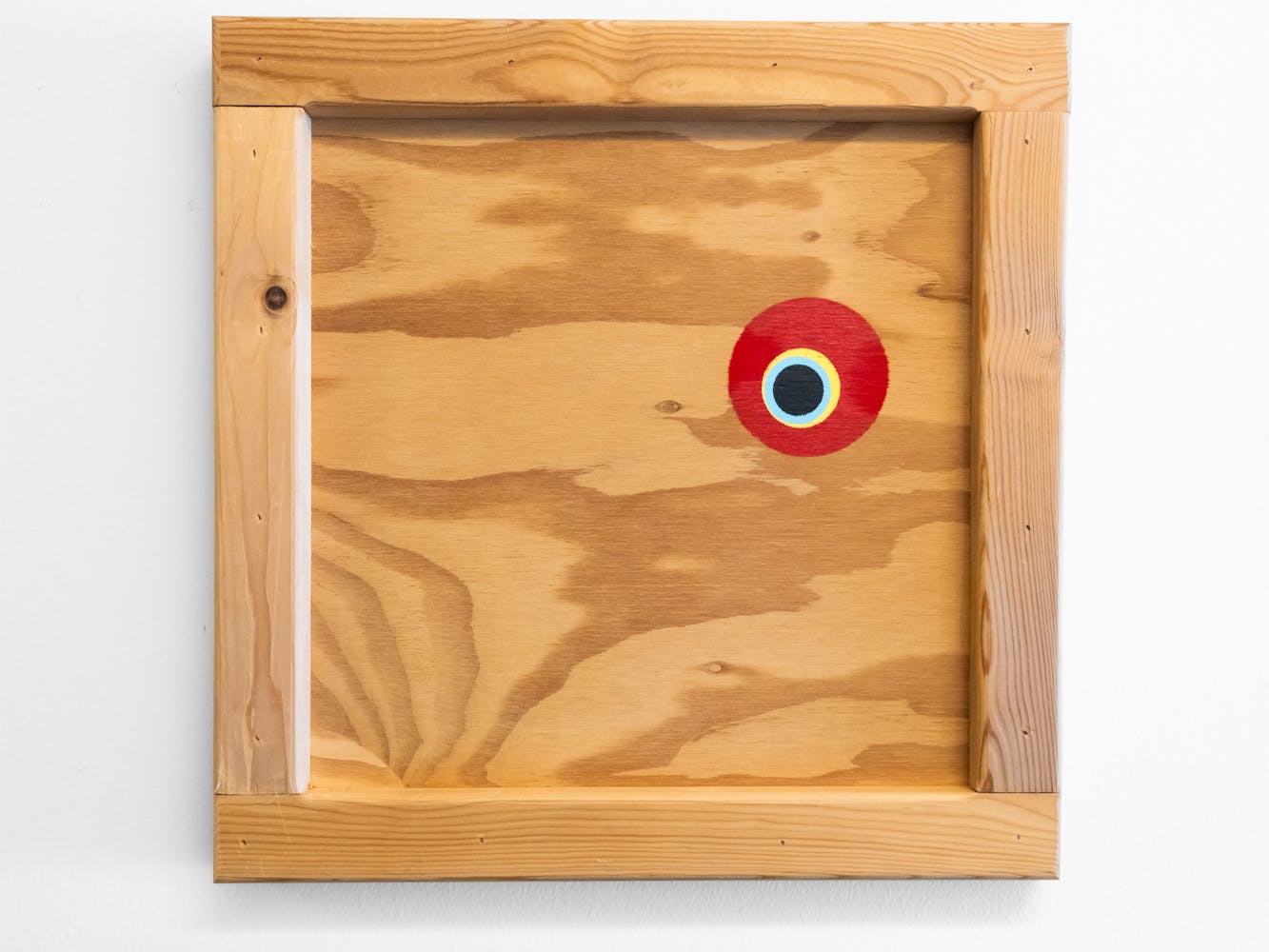 A wood square peice of art with a red and blue painted circle near the top right.