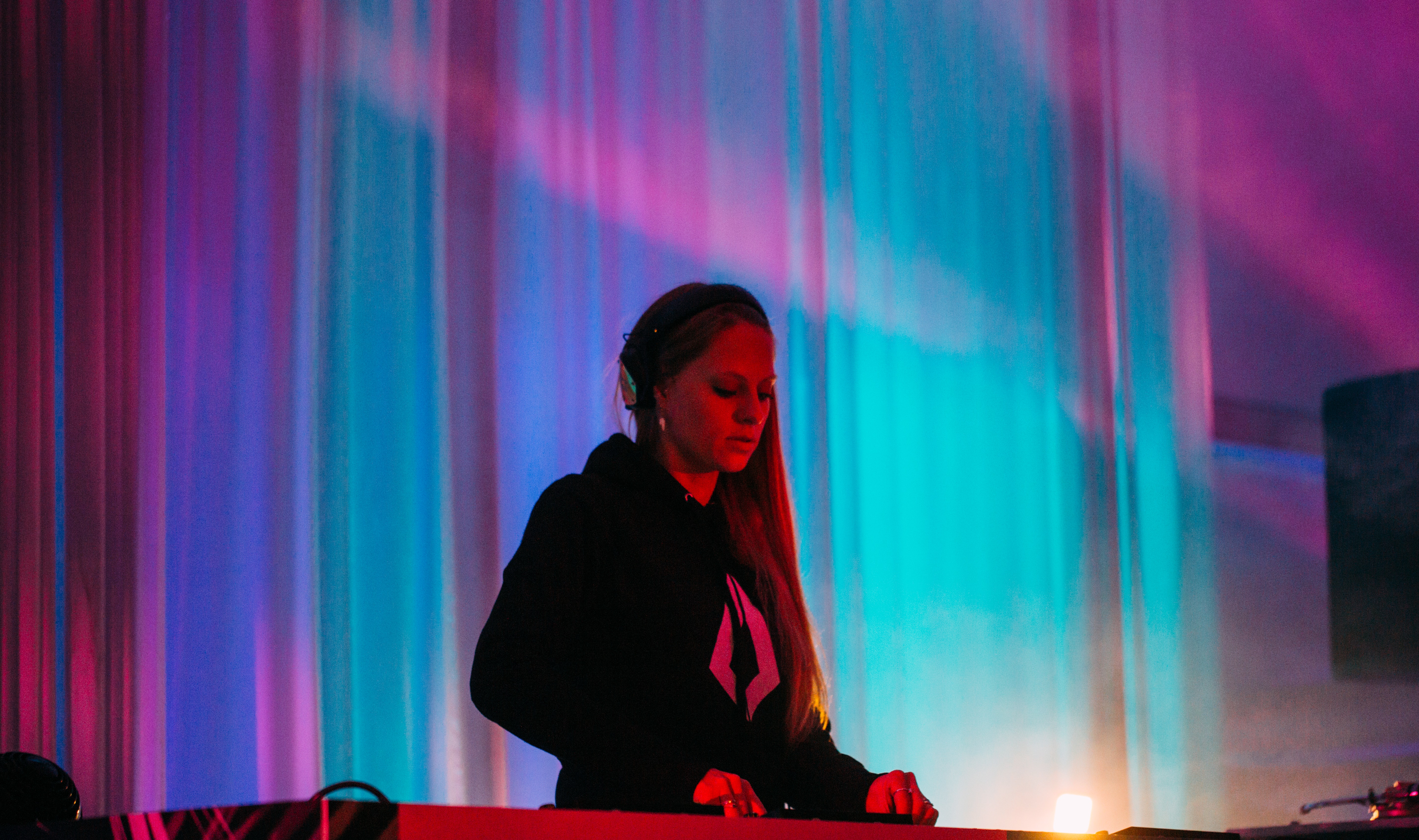 A DJ wearing headphones performs at a mixing console under colorful stage lights.