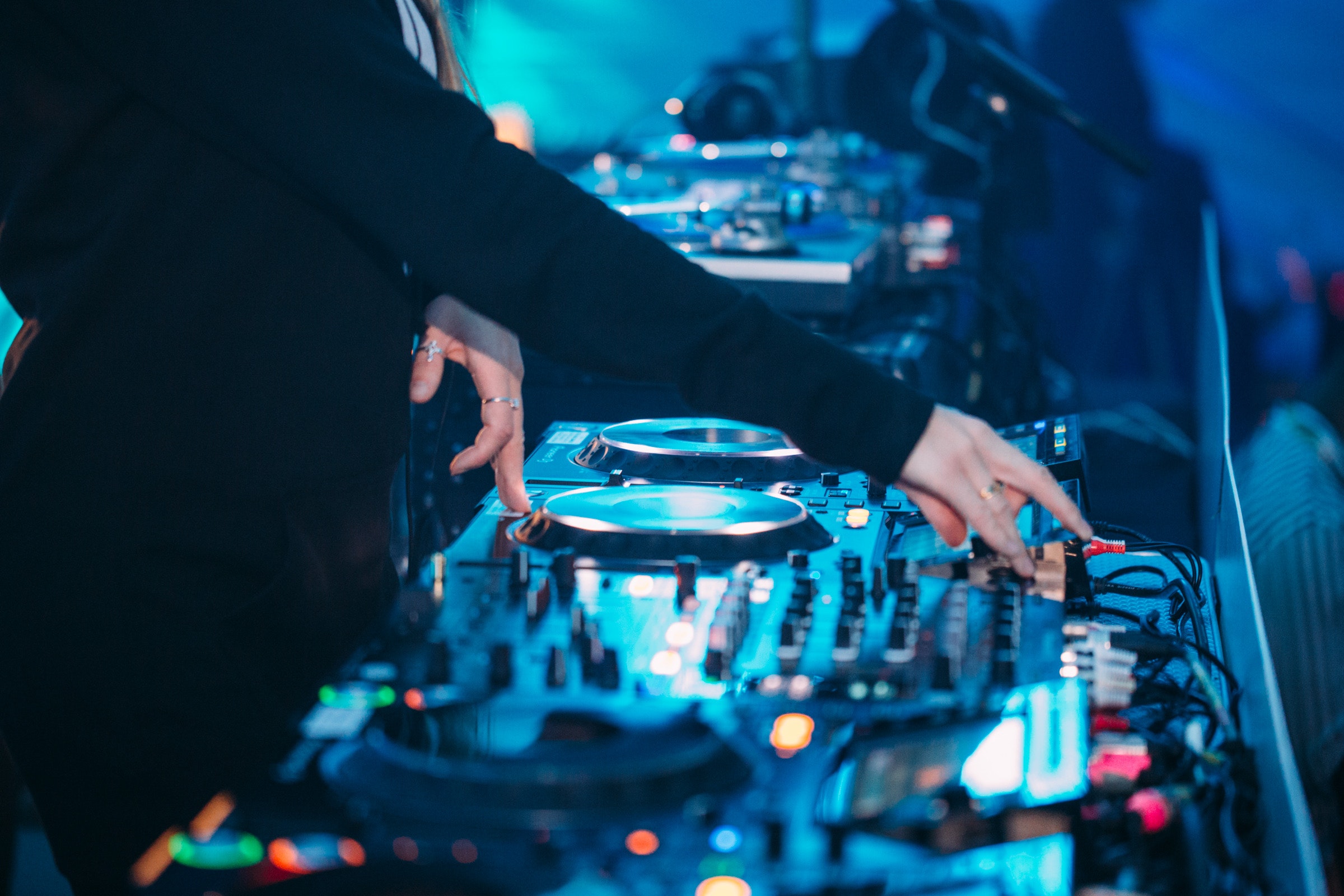 A DJ mixes music on a soundboard with turntables and colorful lights in the background.