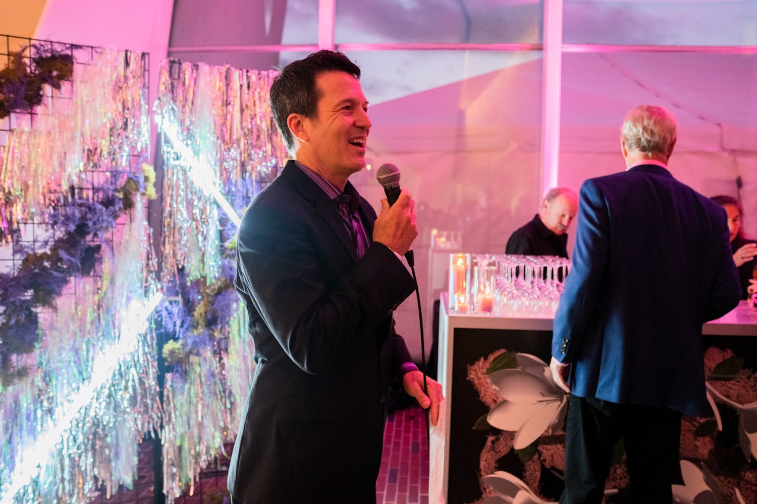 A man in a suite smiles as he speaks into a microphone