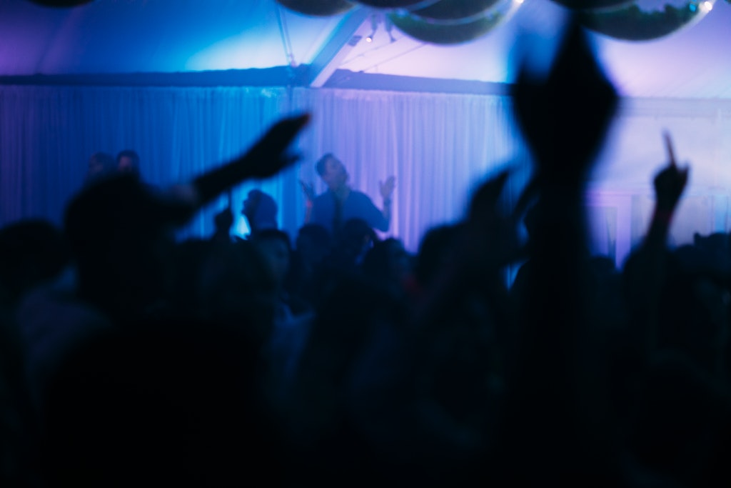 Silhouetted crowd dancing under blue and purple lights at a lively indoor party.