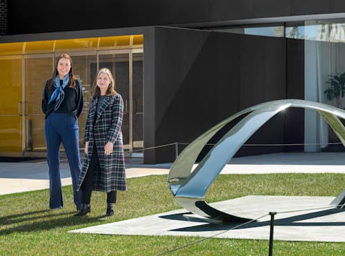 Two women stand next to an outdoor sculpture at the enterance of the the Walker Art Center.