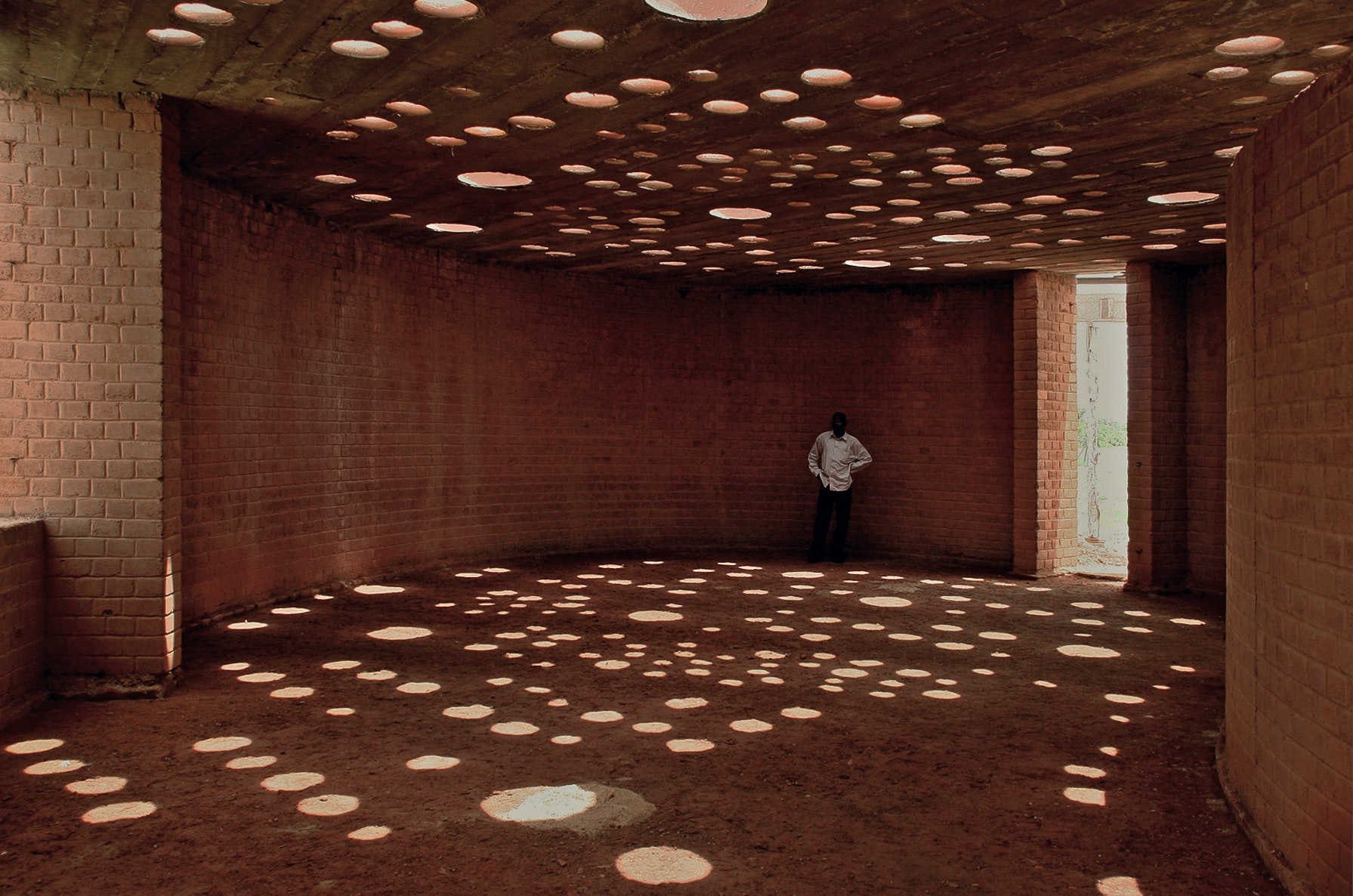 round room with brown walls and circular patterns cut into ceiling allowing sunlight in