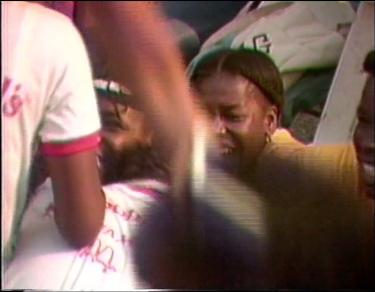 Young people with dark skin in a crowd who appear to be smiling and celebrating. A shadowy blurred shape obscures the image.