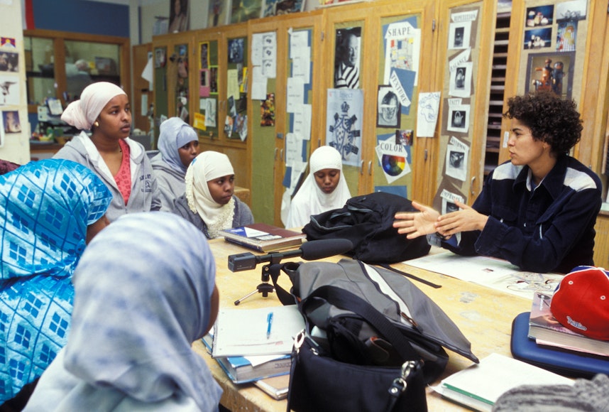 Image of woman teaching students in a classroom with pictures taped on the wall behind