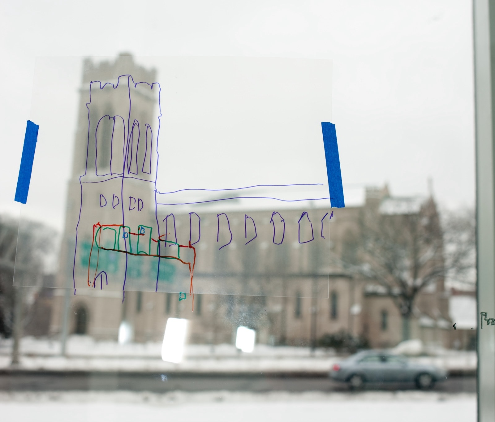 A blurry picture of a building seen from inside a glass window and a sketch drawn over the building on the glass.