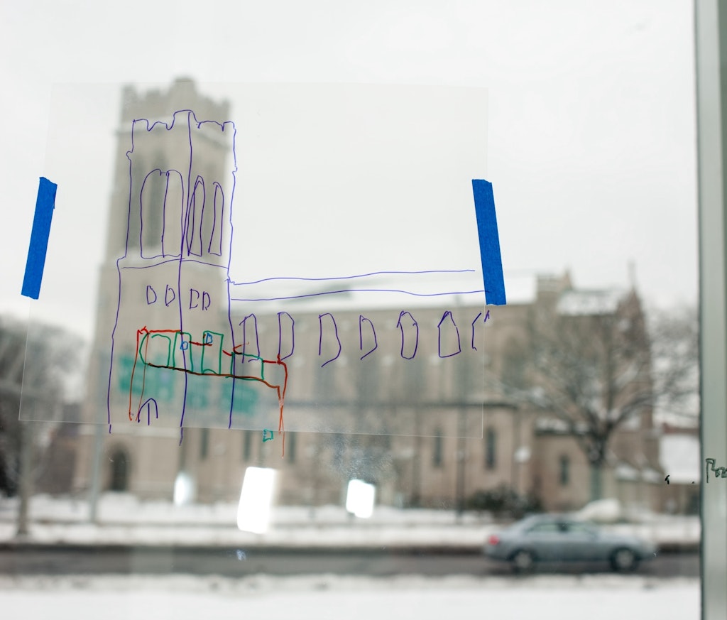 A blurry picture of a building seen from inside a glass window and a sketch drawn over the building on the glass.