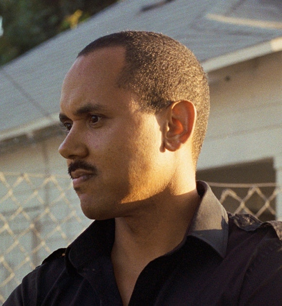 A side portait of an adult with dark skin and a buzz cut and mustache.