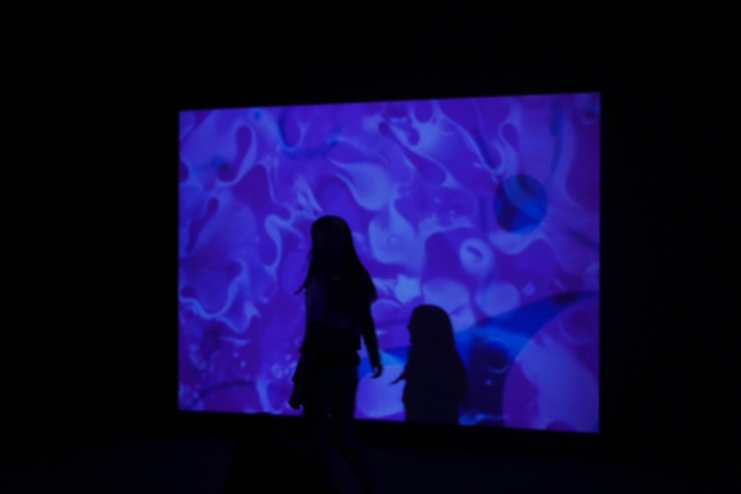 A young woman walks across a projection of moving colors.