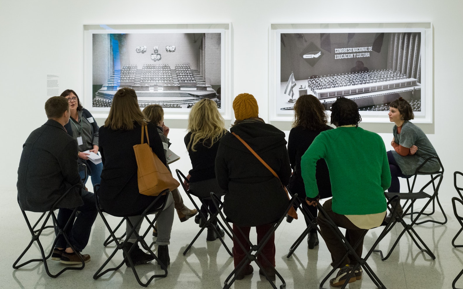 epp2017educators1114_015 A group of adults sit in chairs in front of photographs hung on a gallery wall.