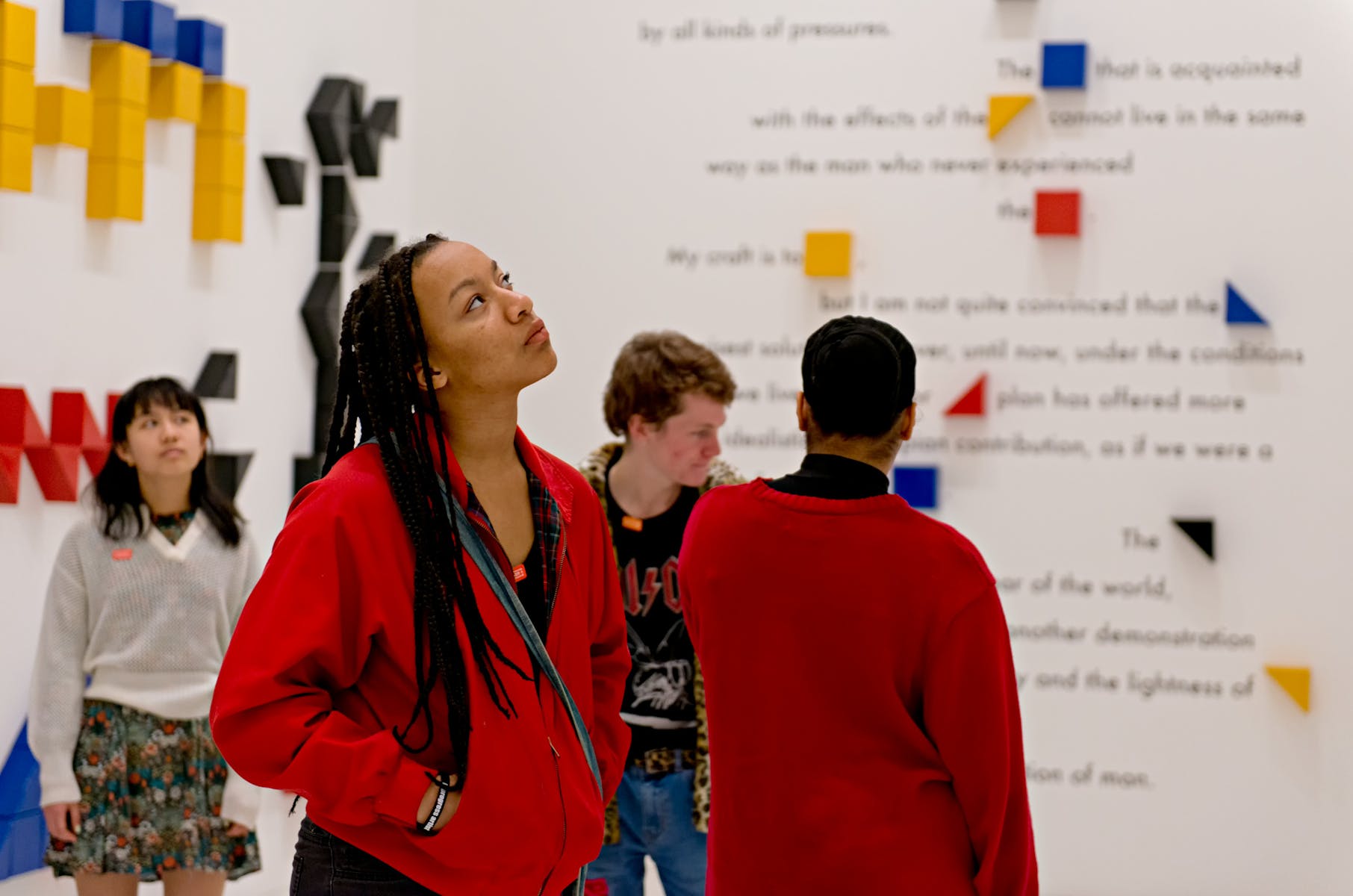 A group of adults and students looks at artwork in a white gallery.