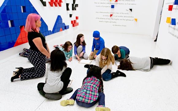 A Group of students with notebooks sitting in a gallery.