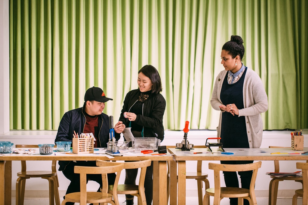 Three adults gathered around a wood table with crafts.