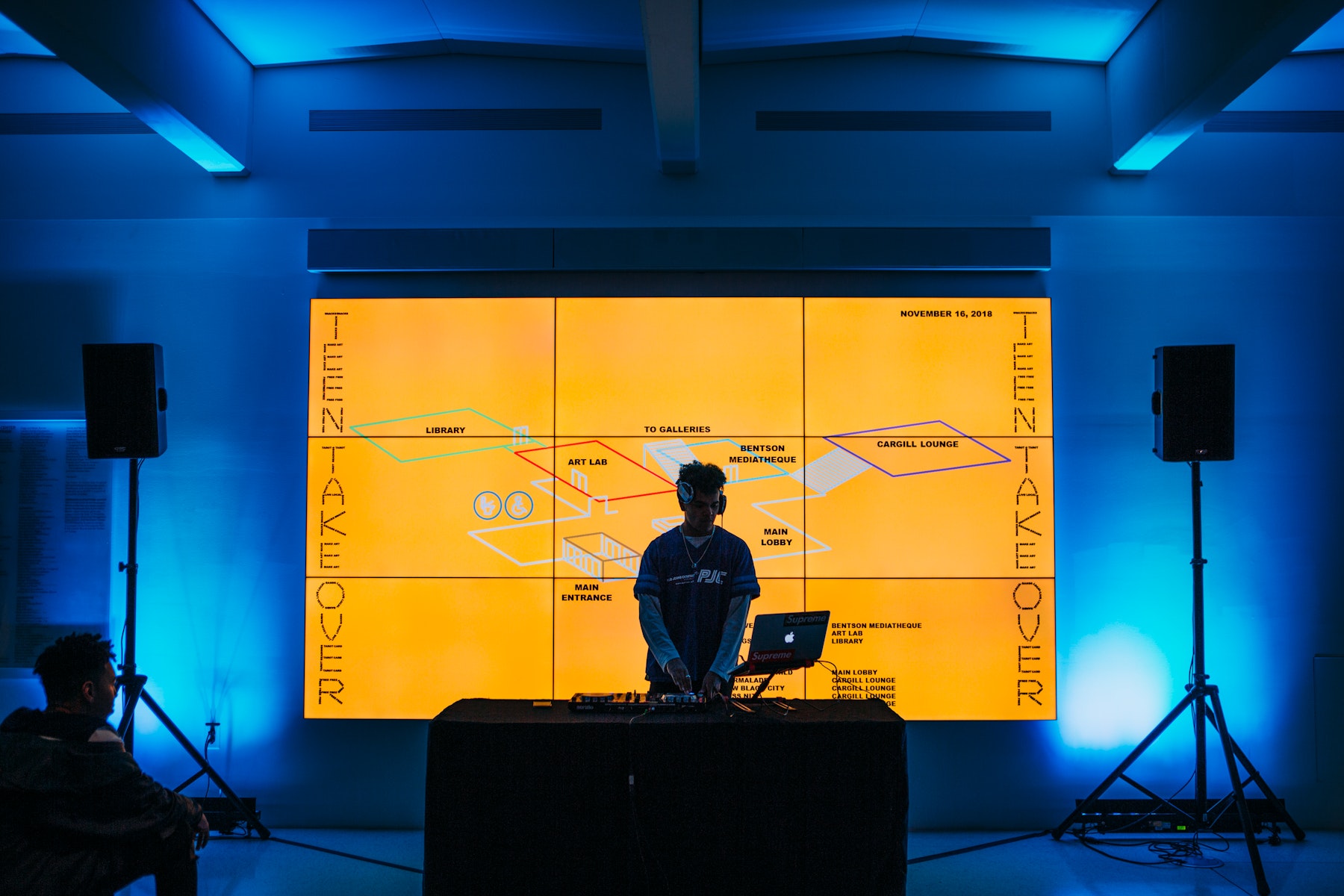 A young man DJ's in front of a wall-sized glowing monitor that reads "teen takeover."