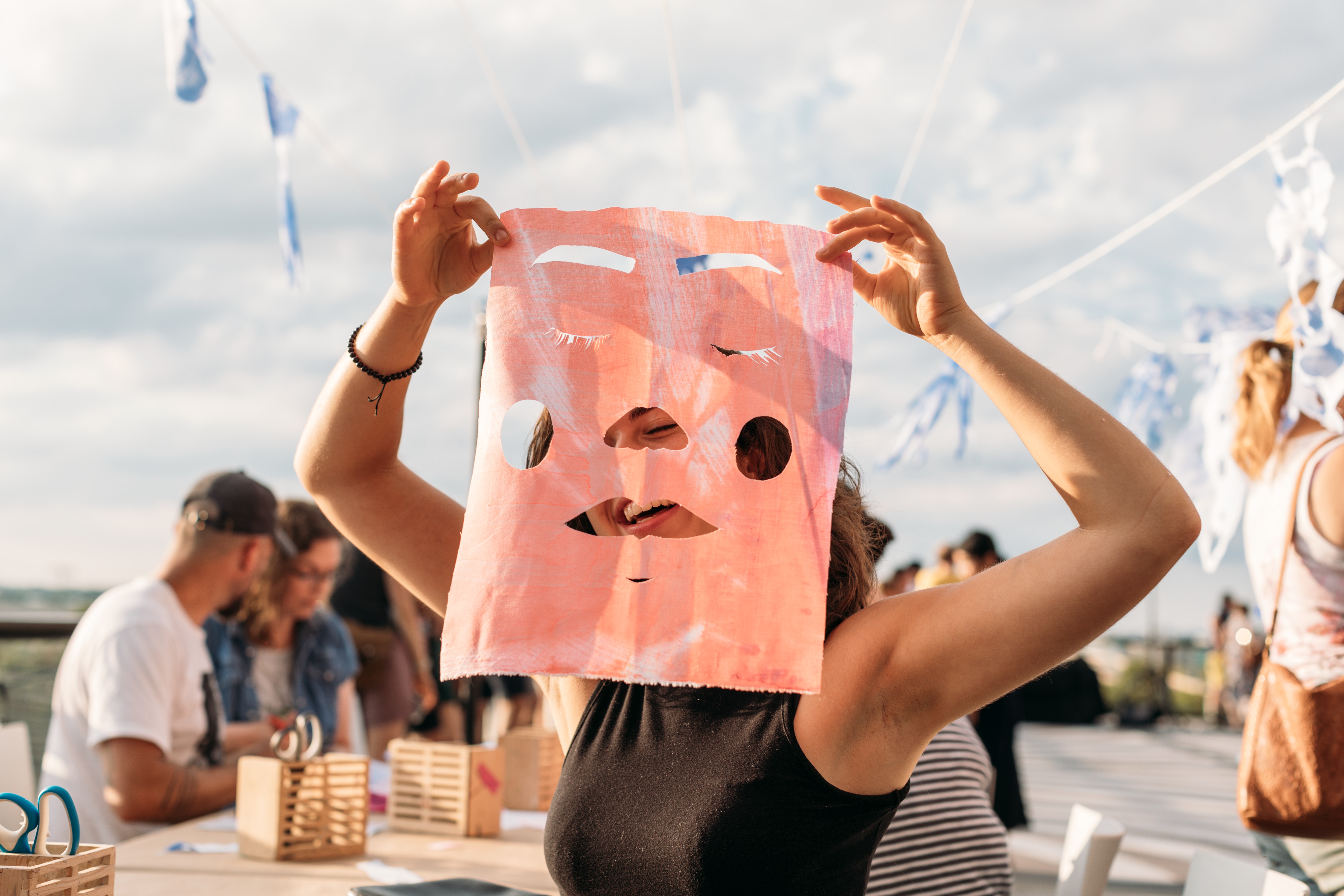 An adult holds up a paper with a cut-out face on it over their face.