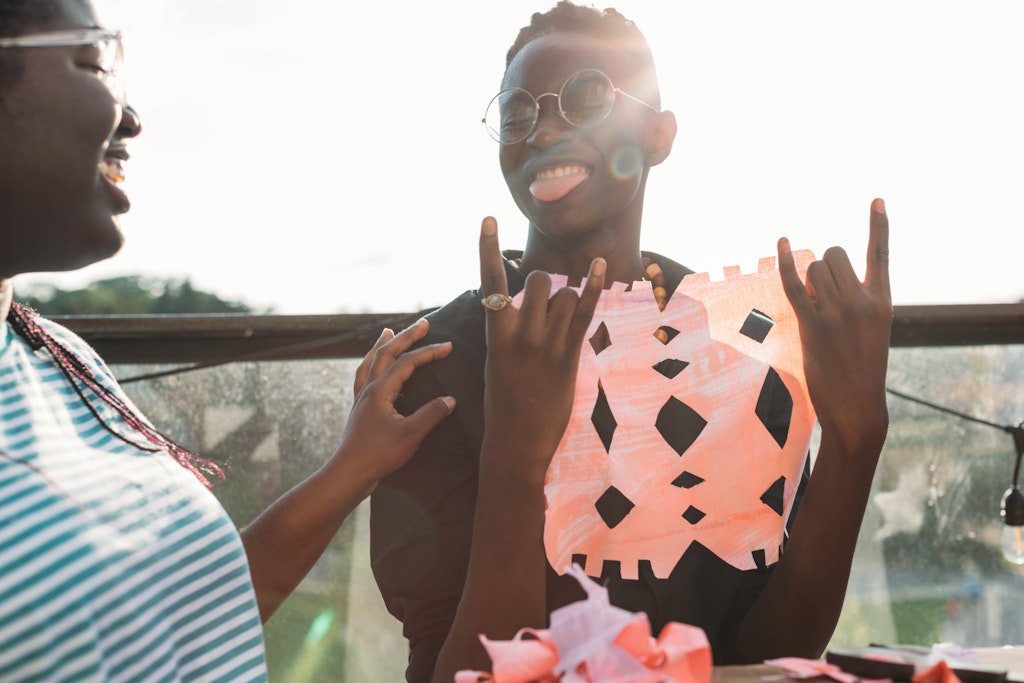 Two adults with dark skin look at eachother, smiling. One has glasses and is holding a paper cut out.