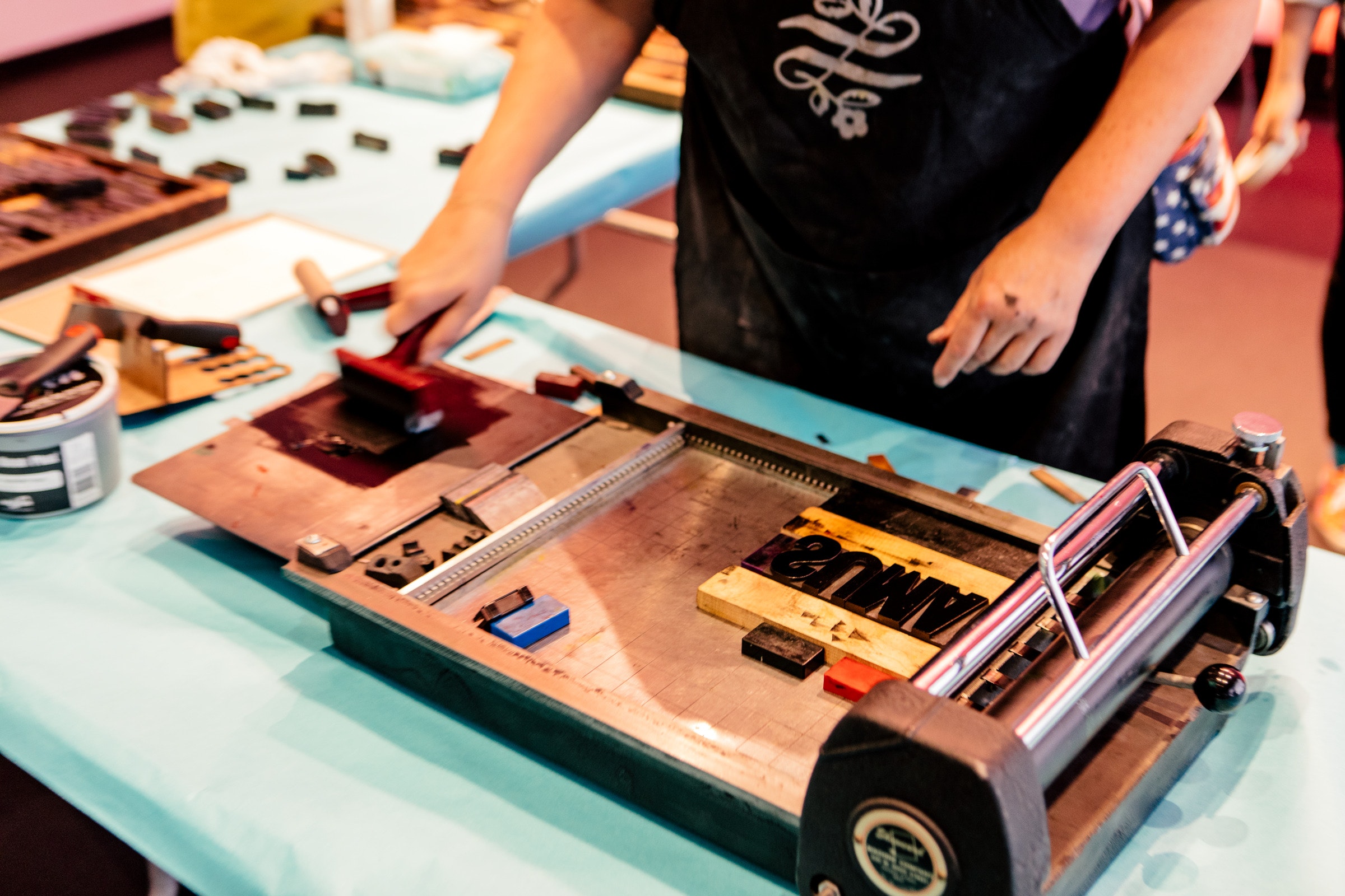 Person rolling ink onto a printing press with woodblocks on a blue table.