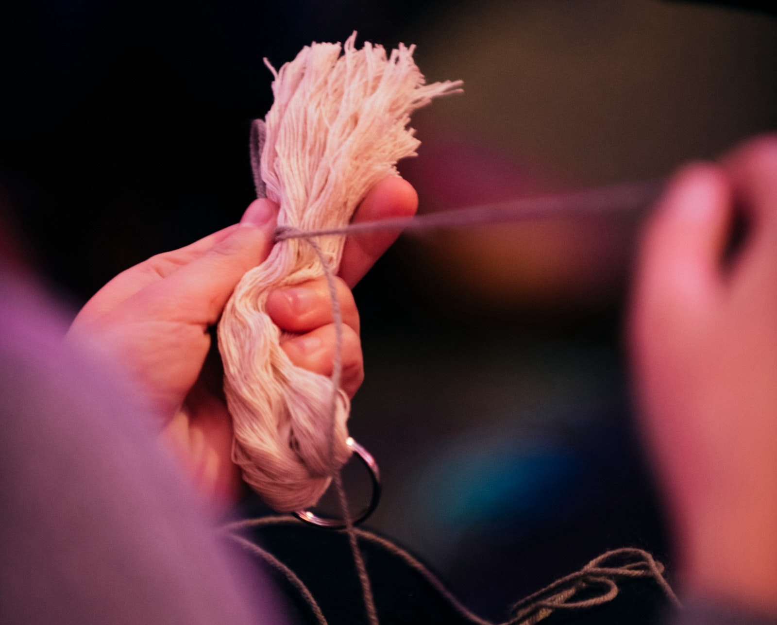 Hands holding a bundle of white yarn and tying purple thread around.