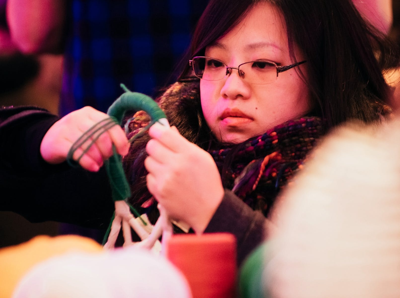 An adult with medium light skin and dark hair and glasses holds a string of green yarn wrapping around a handle.