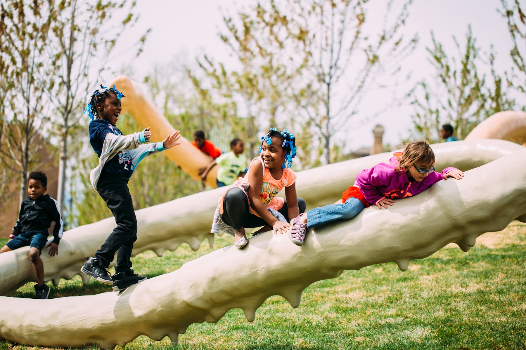A groupd of children plan on large tubular sculpture outside on a sunny day.