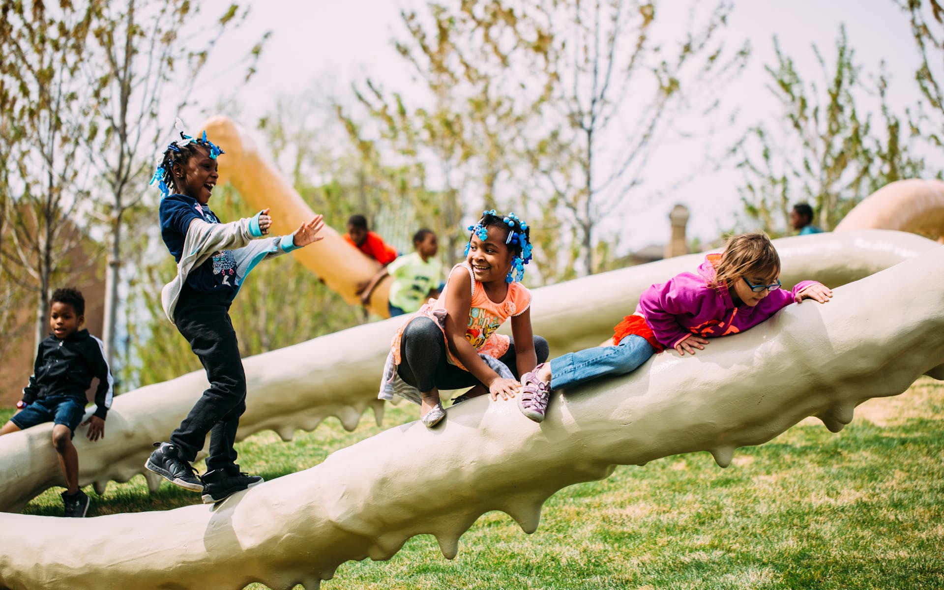 A groupd of children plan on large tubular sculpture outside on a sunny day.