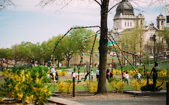 A group of children play in an outdoor sculpture garden with a view of the Minneapolis basilica in the background.