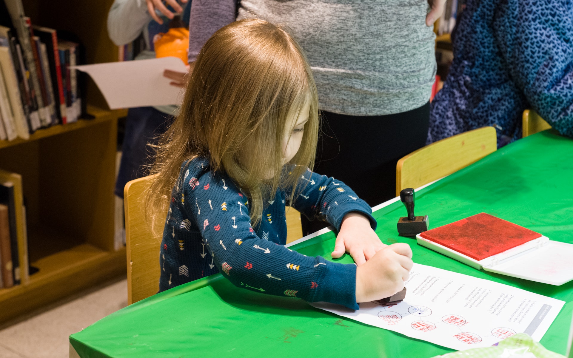 A young girl makes a book at a table using a rubber stamp.