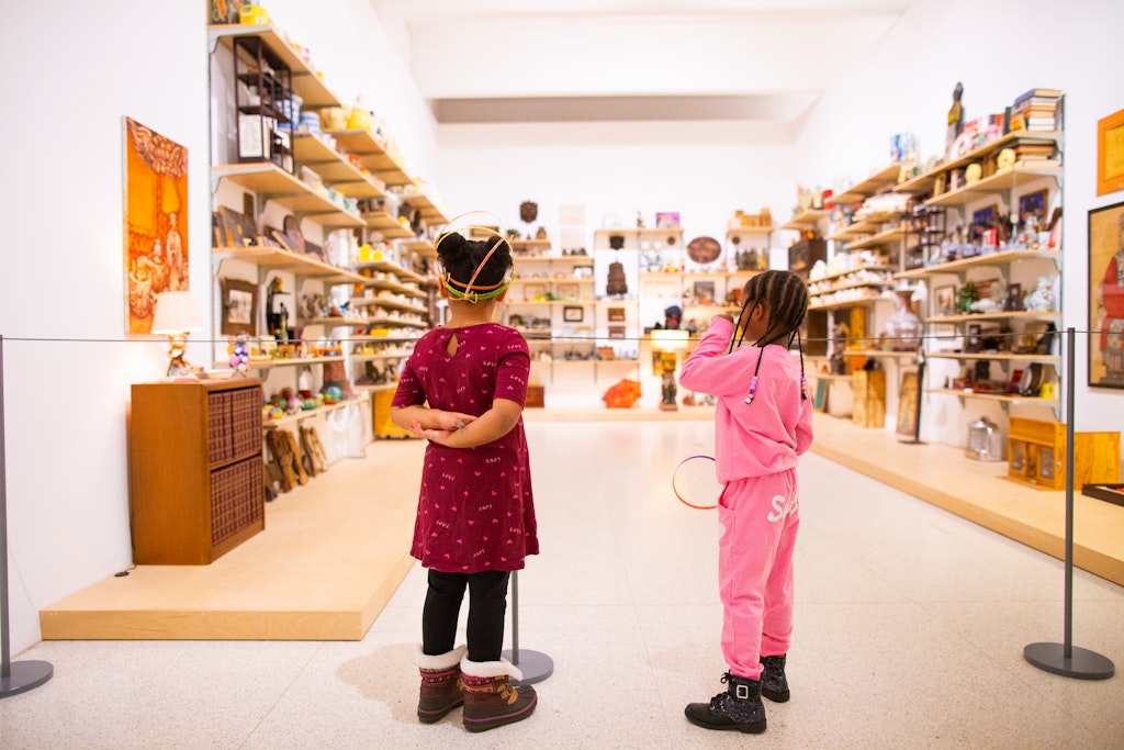 Two children looking at a gallery with shelves on 3 walls full of objects