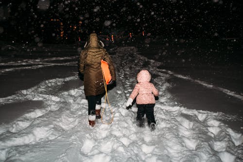 A woman and a child walk thorugh the snow at night.
