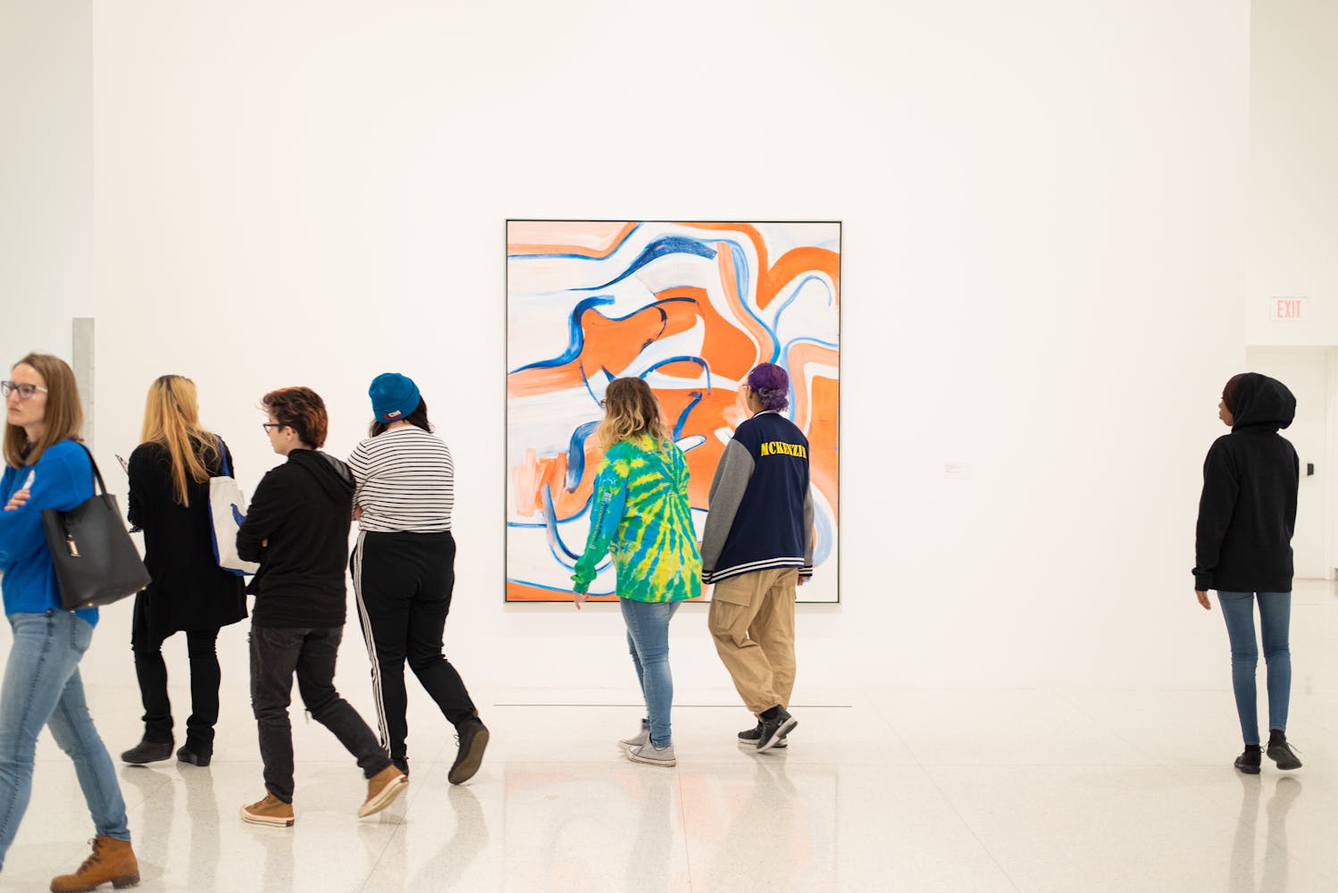 A group of people walk through an art gallery and look at a painting.