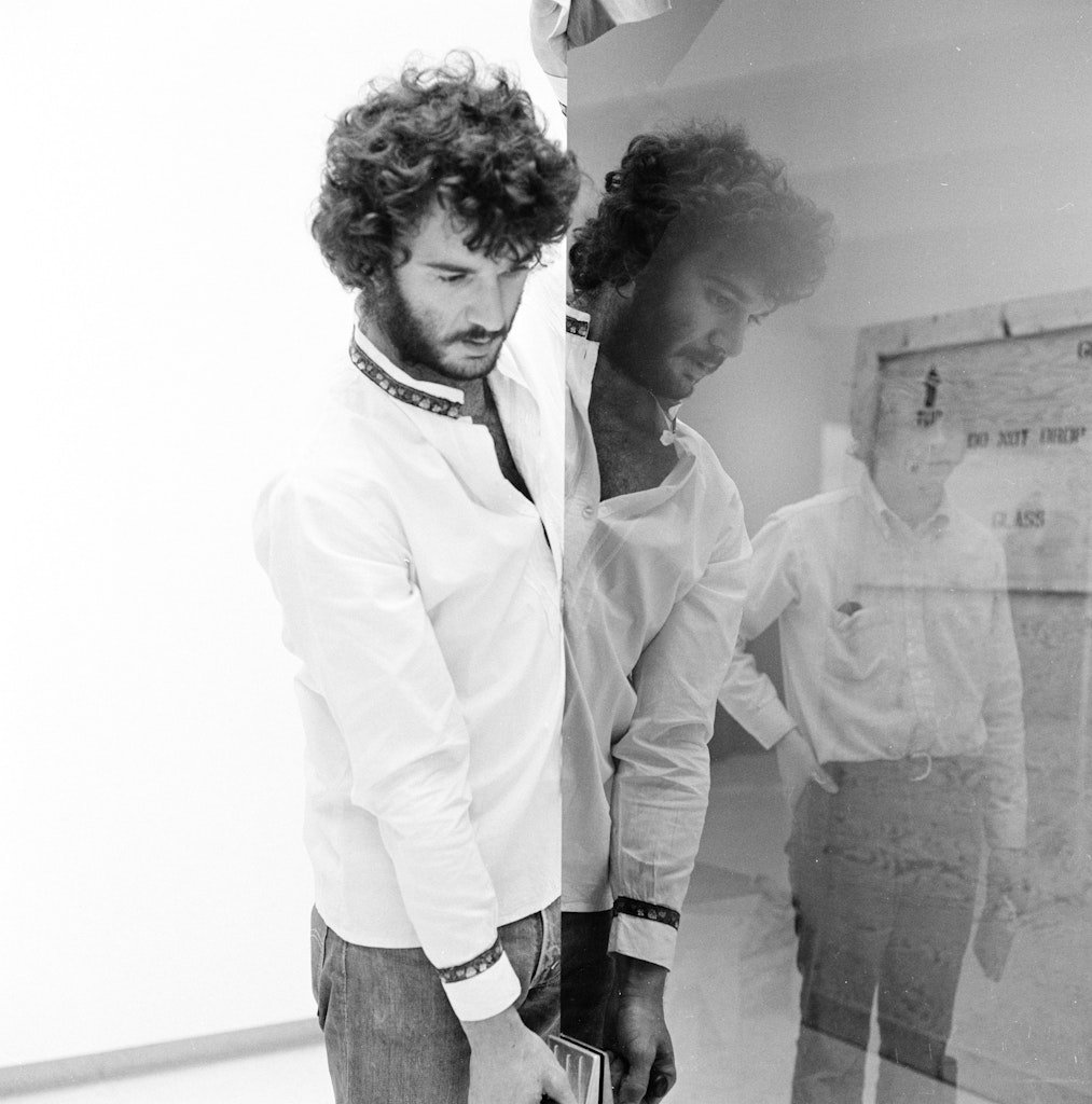 A black and white photo of an adult iwth light skin and curly brown hair holds a mirror