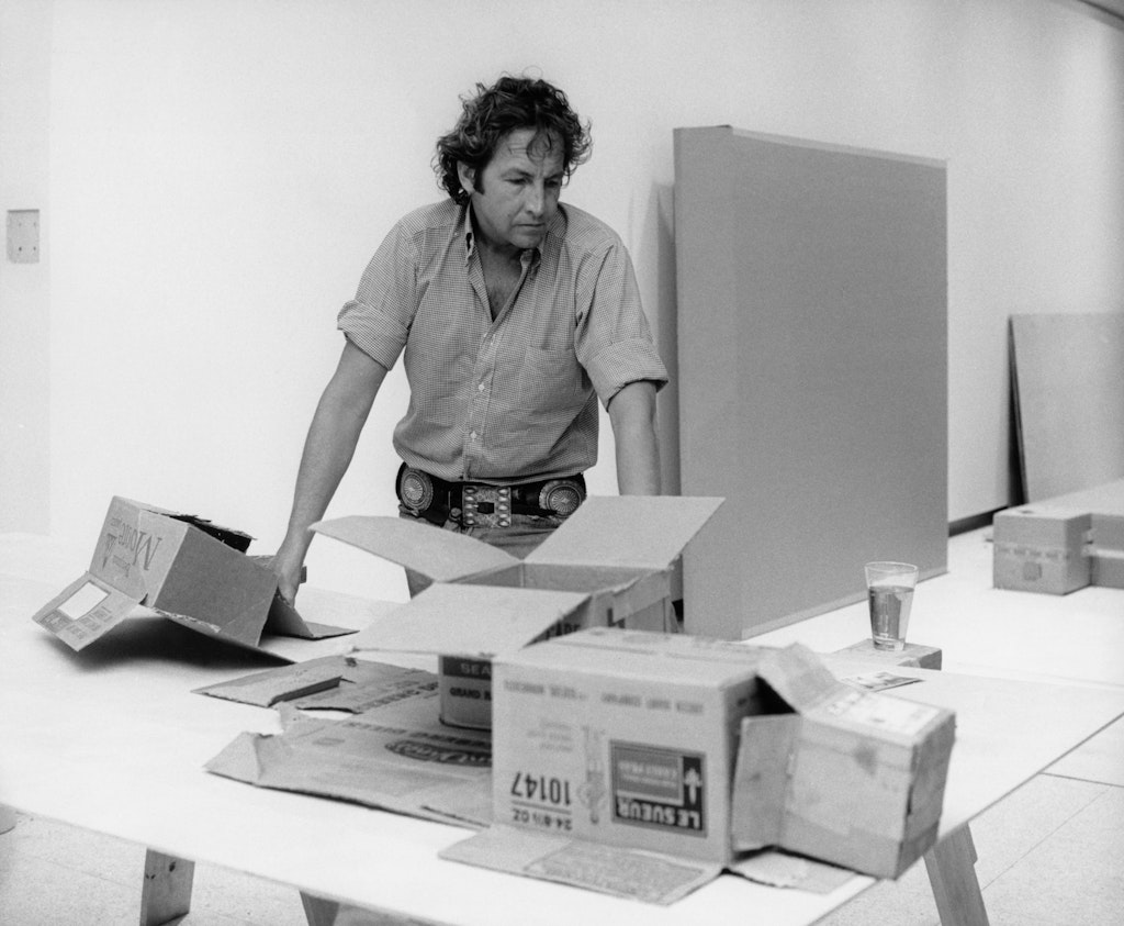 Black and white photo of an adult in a white space with large cardboard boxes around.