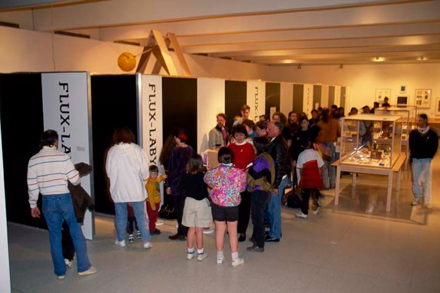Adults and children wait in a long line to enter an artwork hallway in an art gallery.