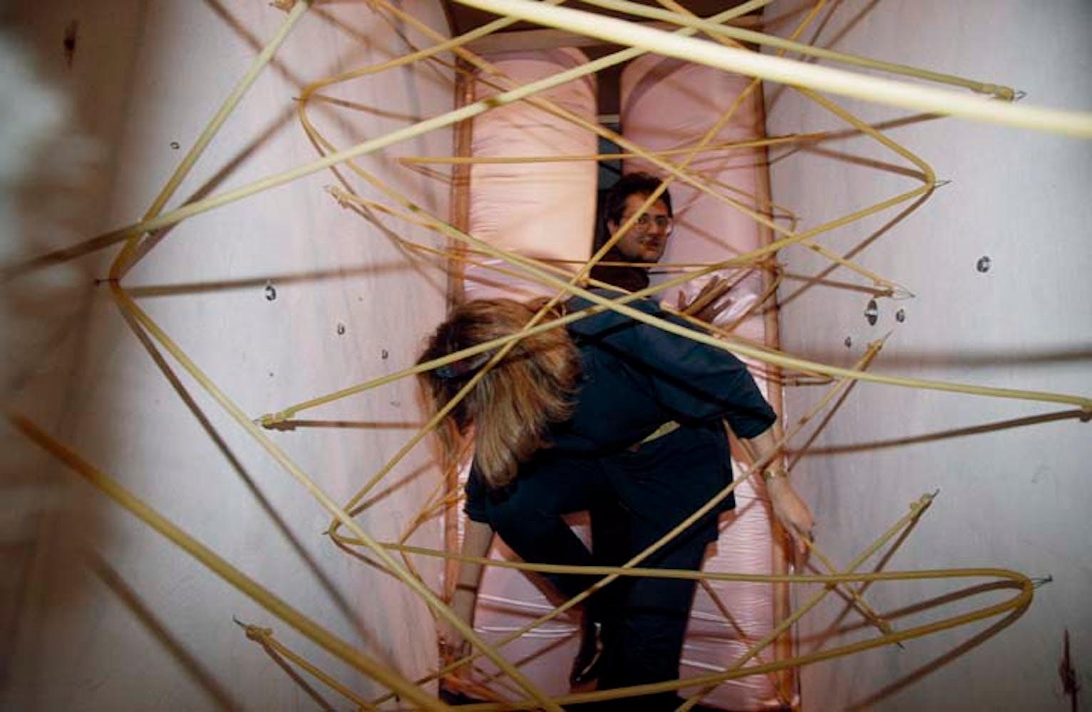 Adults climb through a hallway with frubber tubes streched across the path.