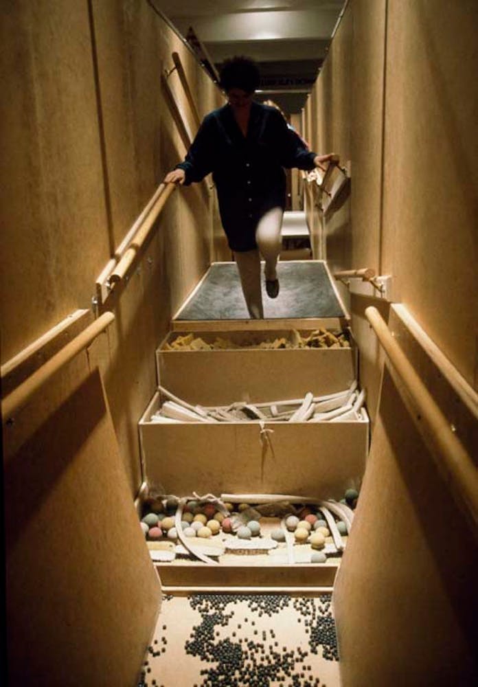 Adults climb through a hallway with floors made of rocks and sand.