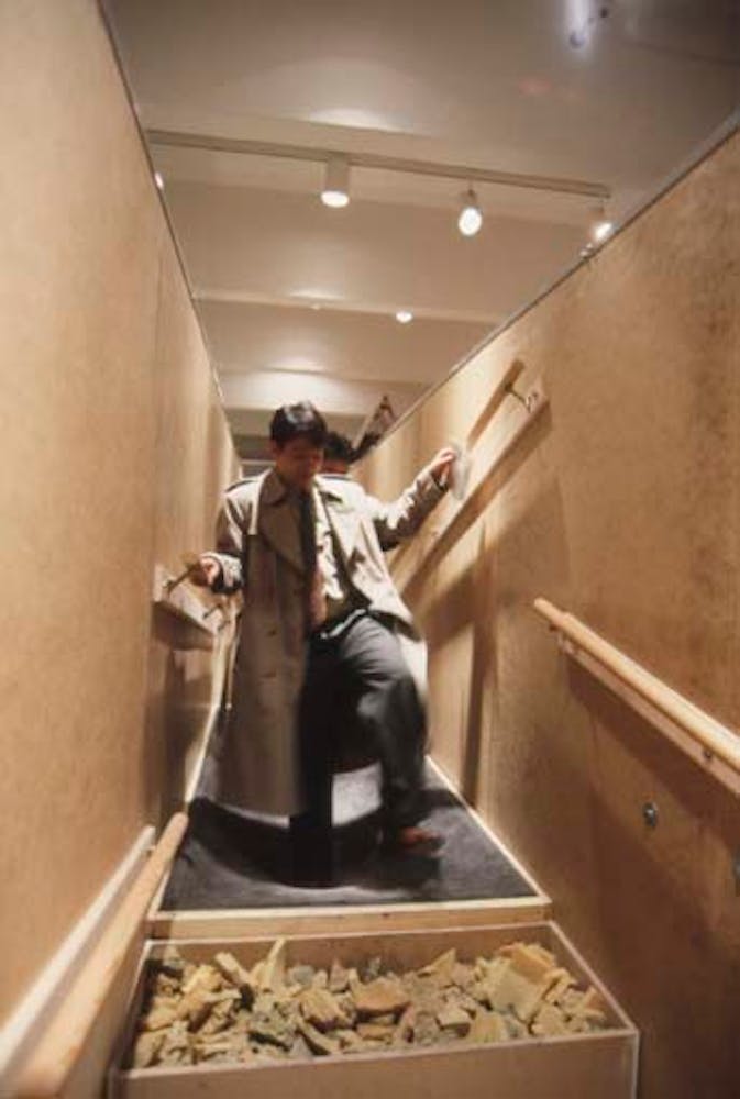 Adults climb through a hallway with floors made of rocks and sand.
